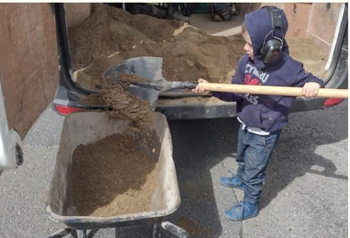 a boy shovelling sand into a van